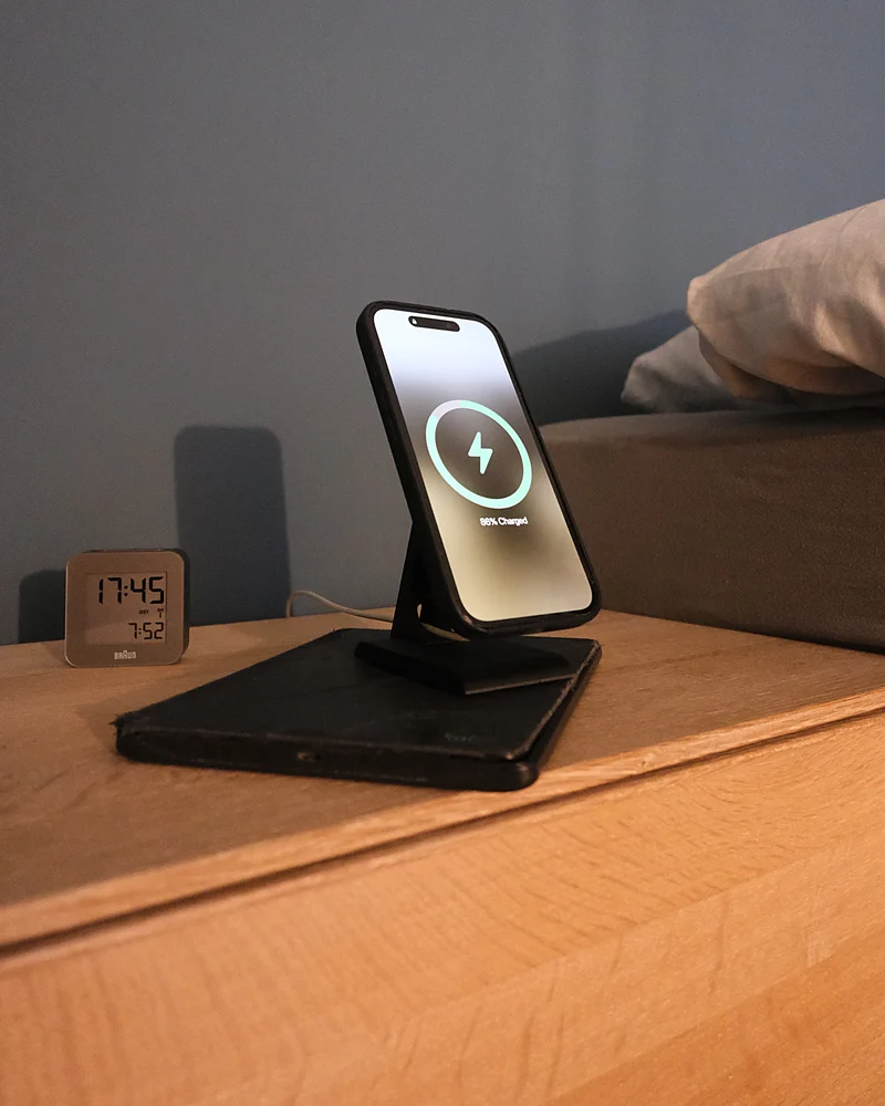 iPhone lädt auf dem HPER, auf einem Nachttisch neben einem Wecker